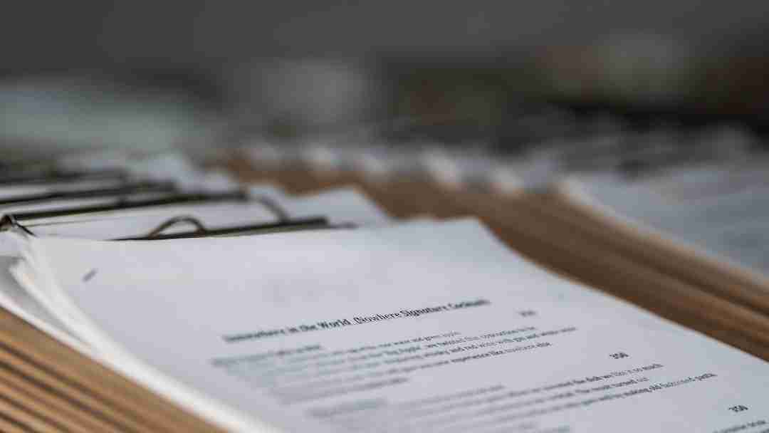 A close-up view of stacks of paper clipped to brown clipboards, with typed text partially visible on the top sheets. The background is blurred, focusing attention on the documents in the foreground.