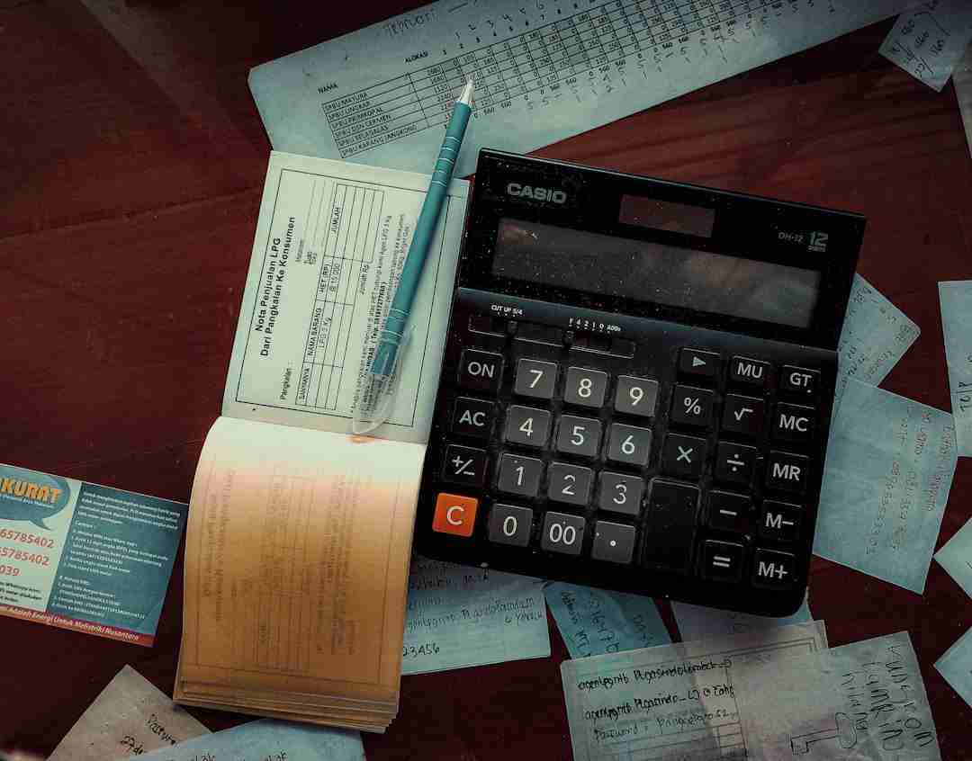 A calculator, pen, business card, receipts, and documents are spread out on a wooden surface, suggesting financial calculations or accounting work.