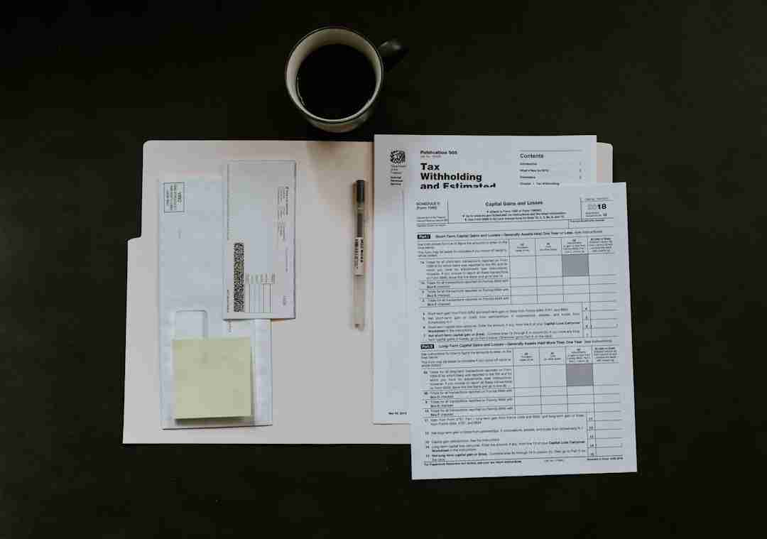 A tax form, envelopes, sticky notes, a pen, and a cup of coffee are arranged neatly on a dark surface. The materials suggest tax preparation or financial paperwork in progress.