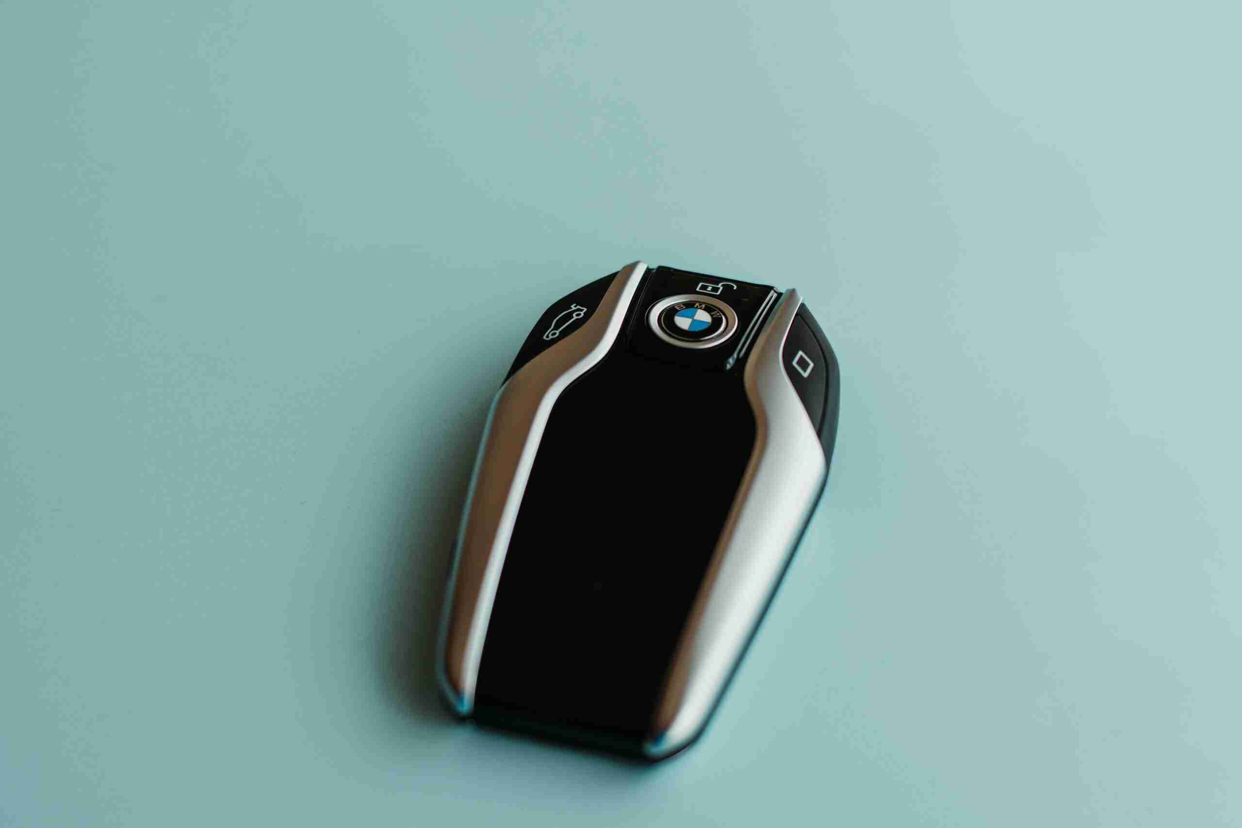 A BMW car key fob with black and silver accents is placed on a plain light blue surface. The BMW logo is visible in the center of the key.