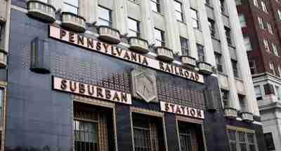 The entrance of Pennsylvania Railroad Suburban Station features an art deco facade with geometric design elements, large windows, and pink signage above the doors.